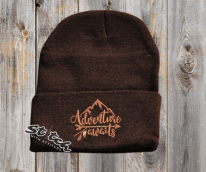 Dark brown beanie with adventure awaits embroidered on it