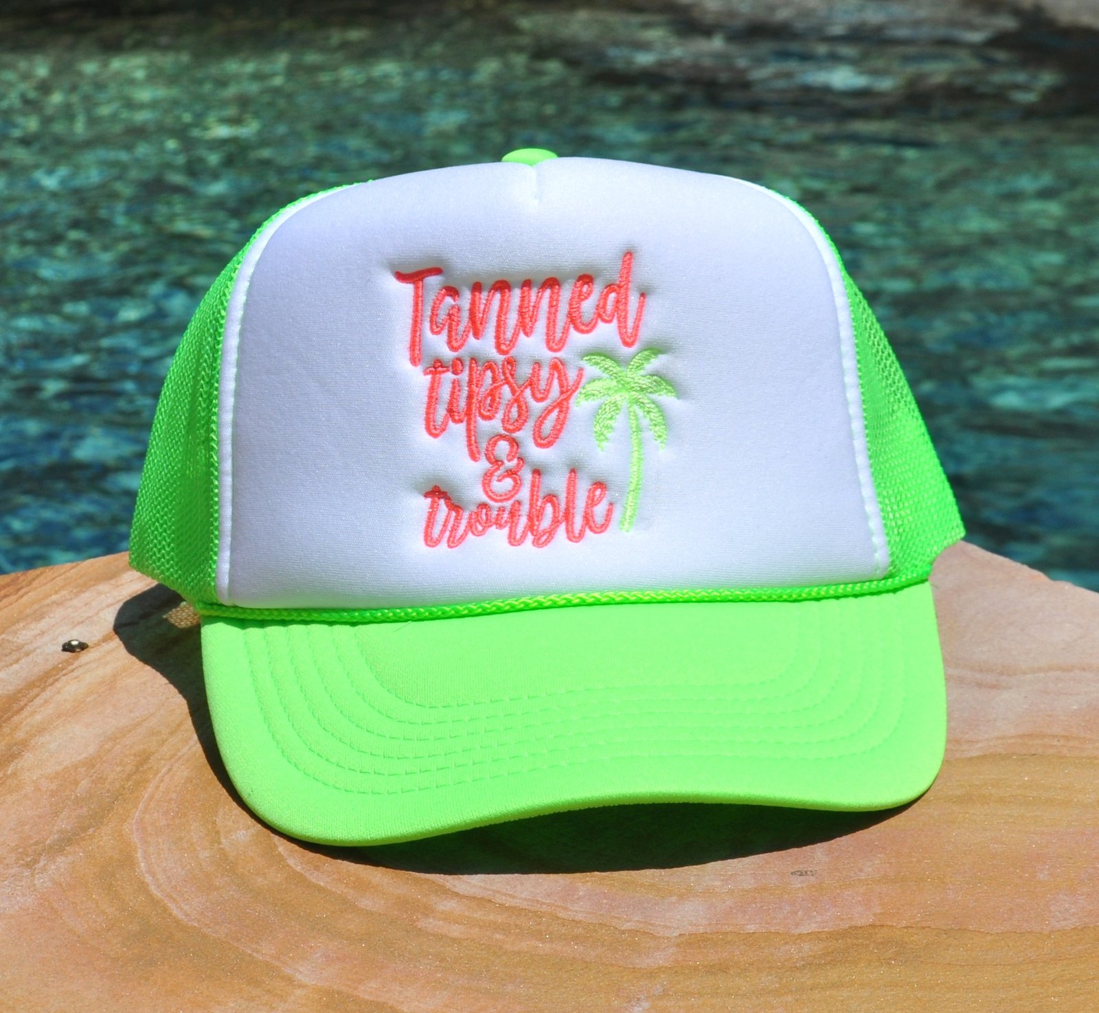 Neon green and white foam trucker hat with "Tanned, Tipsy and Trouble" embroidered on the front