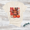Highland Cow Fall Pumpkin Rhinestone Tee. A shaggy little cow in a plaid bow, three pumpkins, and real rhinestones set by hand. Fall, wearing it loudly.