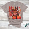 Highland Cow Fall Pumpkin Rhinestone Tee. A shaggy little cow in a plaid bow, three pumpkins, and real rhinestones set by hand. Fall, wearing it loudly.