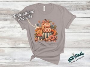 Stacked Pumpkins Fall Tee with Rhinestone Accents - Stacked-Pumpkins-Rhinestone-Tee-1.jpg Stacked Pumpkins Fall Tee with Rhinestone Accents. Three painted pumpkins under a gingham bow, with mushrooms, sunflowers and stars, and real rhinestones set by hand across the des