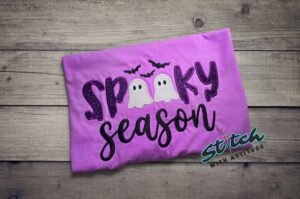 Spooky Season Glitter Ghost Applique Tee. SPOOKY in dark purple glitter, two little glitter ghosts standing in for the double O, and Season stitched in script underneath. Bats incl