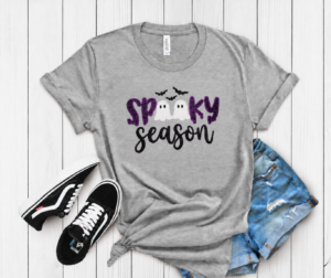 Spooky Season Glitter Ghost Applique Tee. SPOOKY in dark purple glitter, two little glitter ghosts standing in for the double O, and Season stitched in script underneath. Bats incl